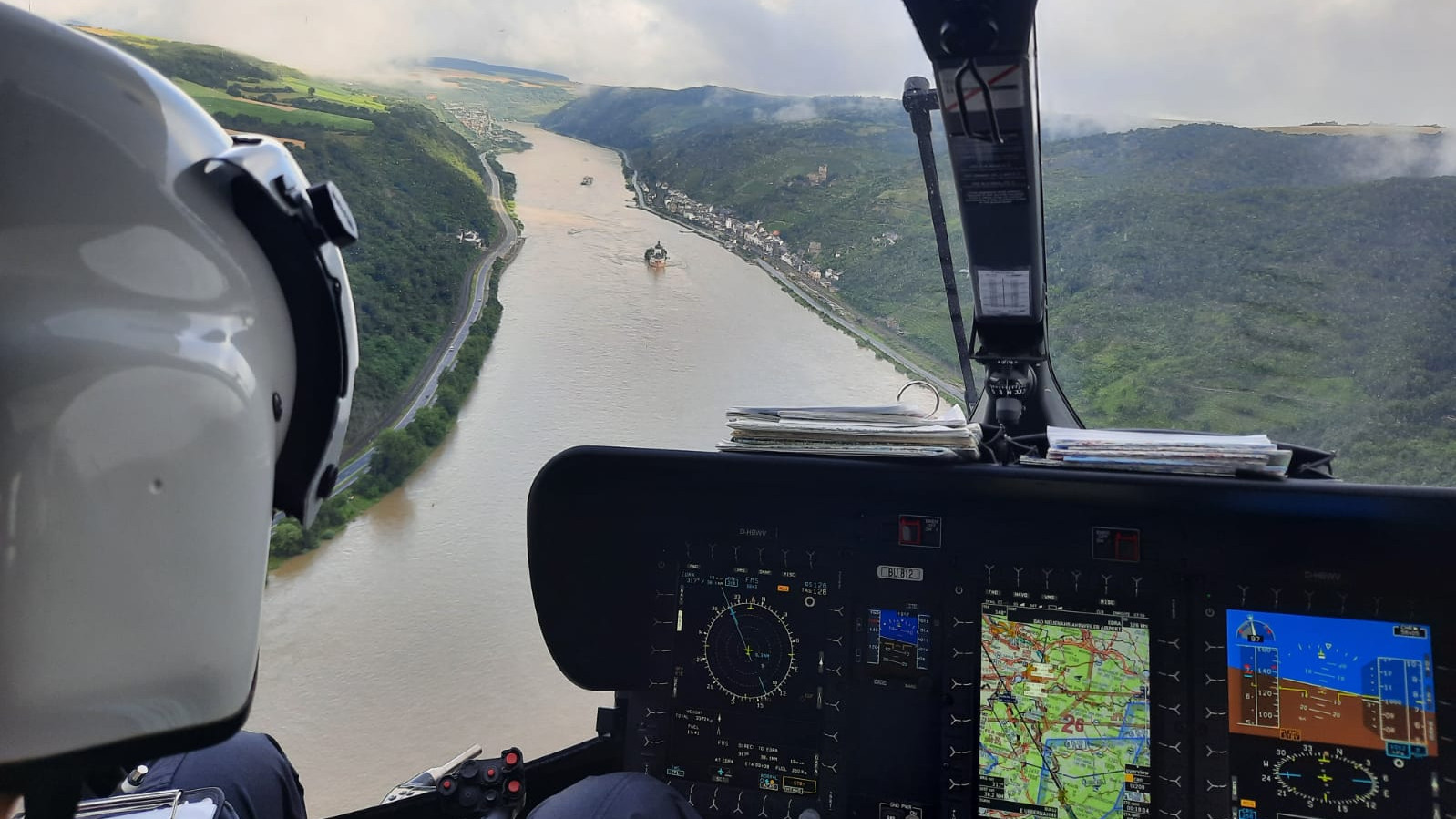 Blick aus dem Cockpit eines Hubschraubers auf einen überschwemmten Fluss.